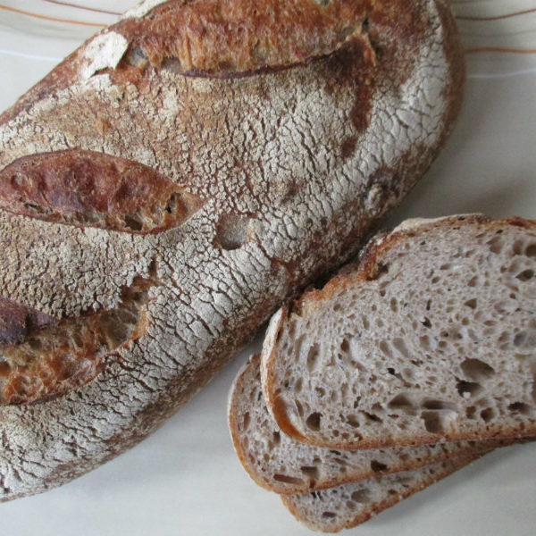 An oval loaf of Black Bean Sourdough with three slices next to it