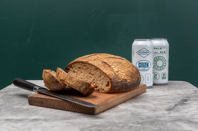 Citizen Sourdough A round loaf of sourdough on a chopping board with two slices cut and two cans of beer beside