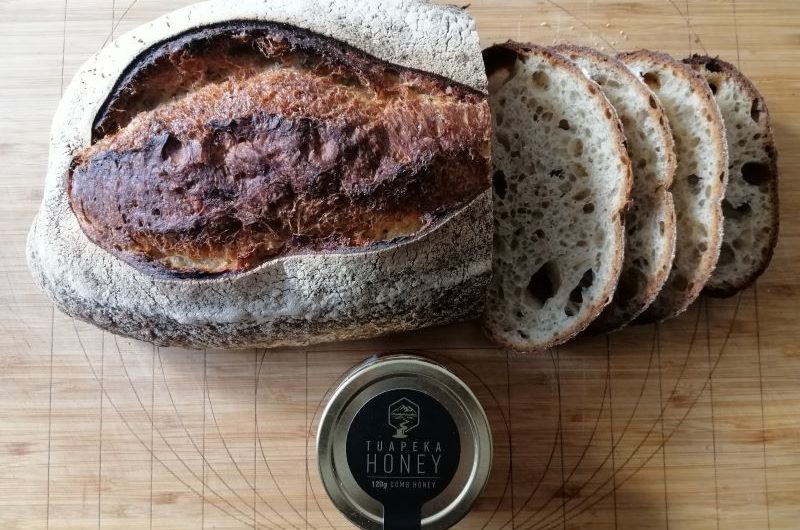 Kawakawa and Honey Sourdough A loaf of sourdough with a third in slices and a jar of honey in front