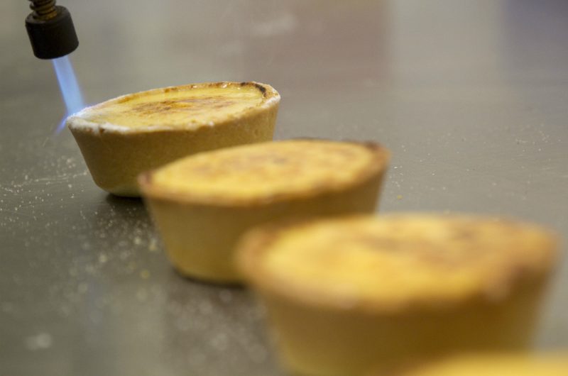 Three brulee tarts in a row, the last one in focus under the blowtorch